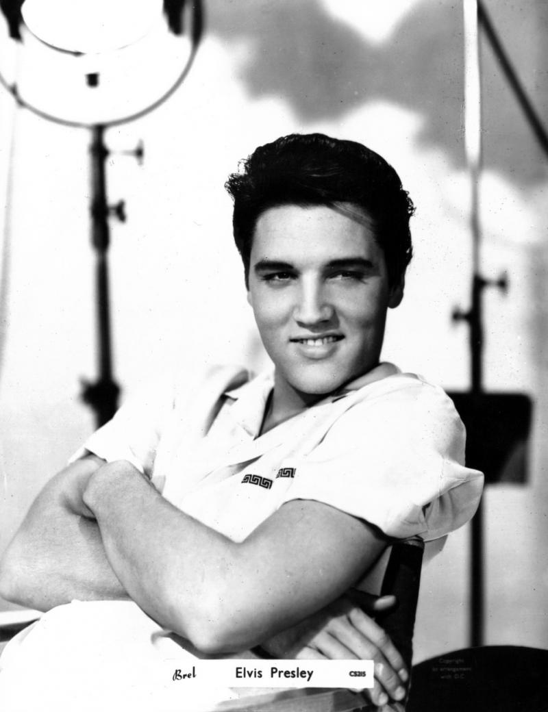 Elvis Preasley este așezat pe scaun și zâmbește