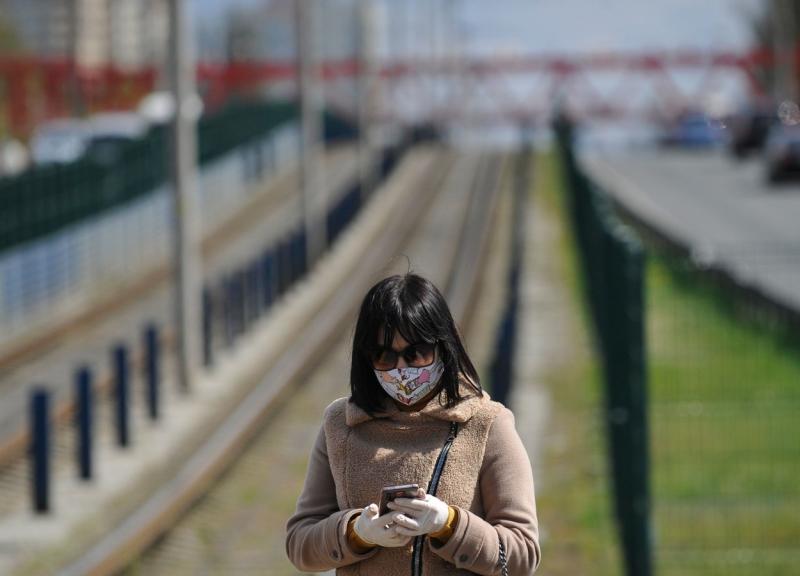 Femeie cu mască privește telefonul într-o stație de tramvai din Kiev