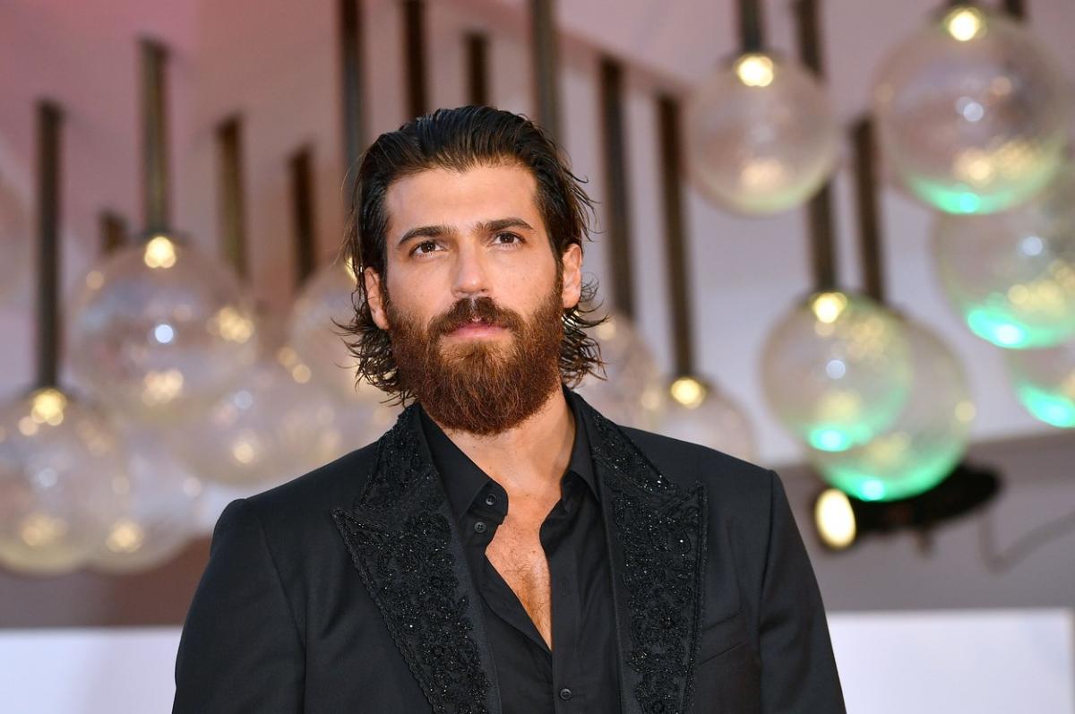 Can Yaman poartă o ținută all-black și are părul dat pe spate. Actorul are barbă