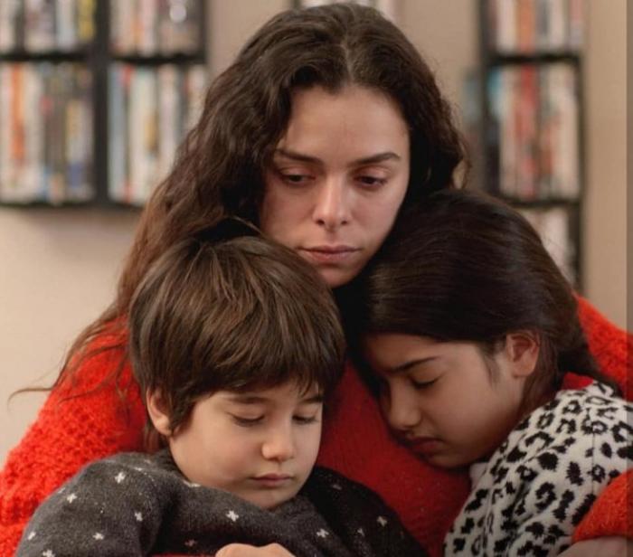 Bahar poartă o bluză roșie și îi ține în brațe pe cei doi copii