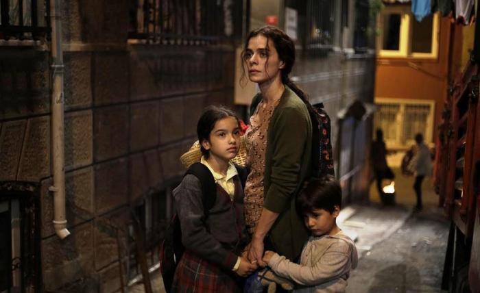 Bahar este alături de cei doi copii pe care îi ține aproape de trup. Poartă părul prins în coadă și are haine închise la culoare