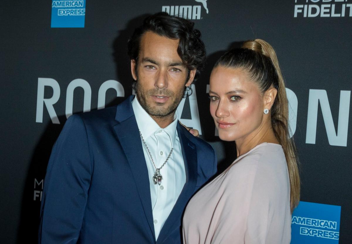 Aaron Diaz poartă o cămașă albă și un sacou albastru și are părul scurt