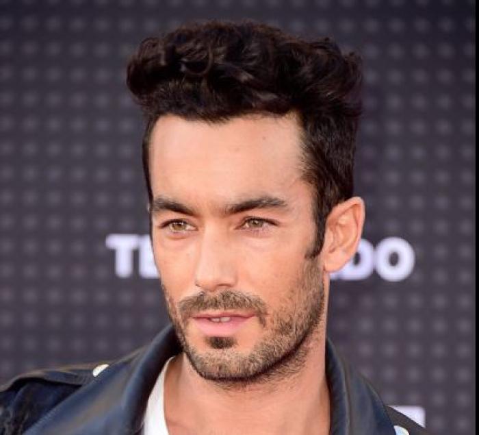 Aaron Diaz poartă părul scurt și ondulat și are barbă
