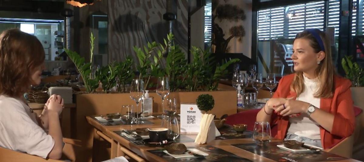 Eli poartă o bluză albă și un sacou portocaliu