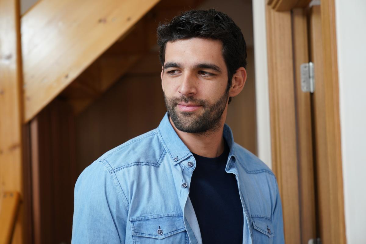 Melih Özkaya poartă un tricou albastru închis și o cămașă albastru deschis