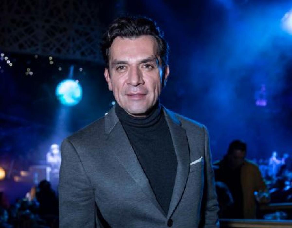 Jorge Salinas poartă un costum închis la culoare și o maletă neagră
