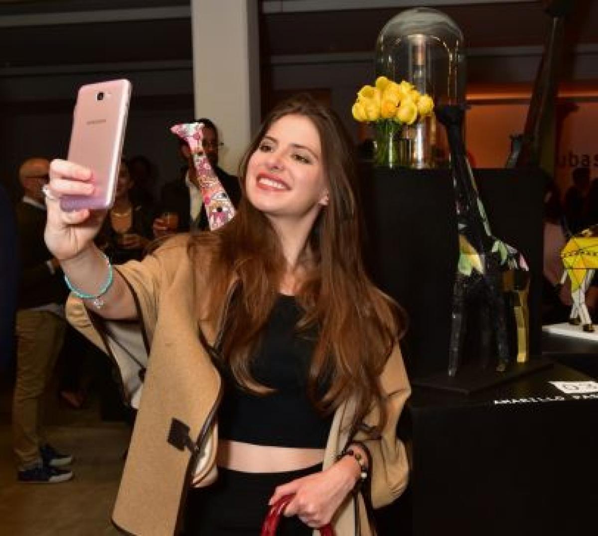 Daniela Aedo poartă pantaloni negri, bluză neagră și o jachetă maro deschis. Actrița are în mână o geantă roșie