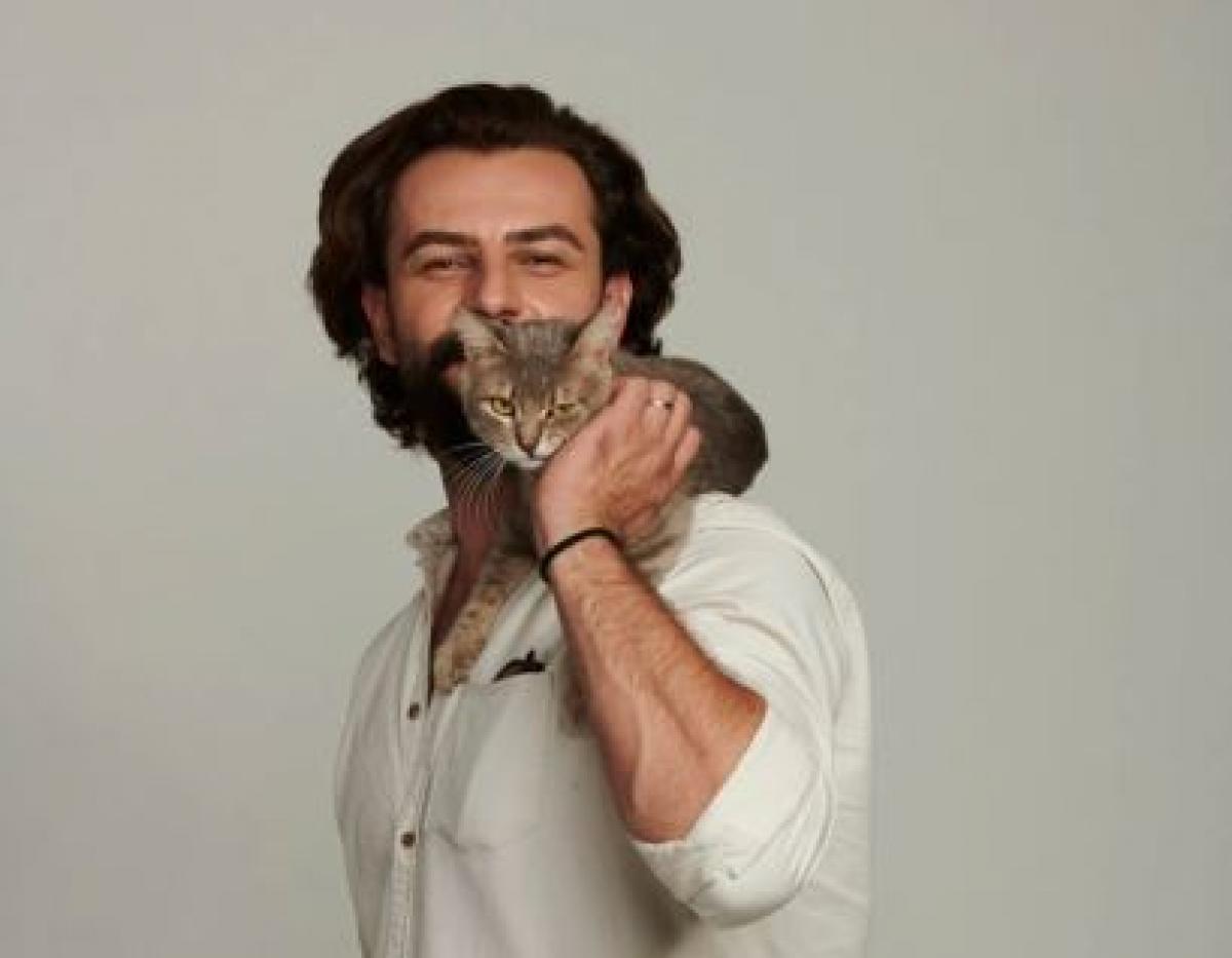 Gokberk Demirci poartă o cămașă albă și are o pisică pe umăr