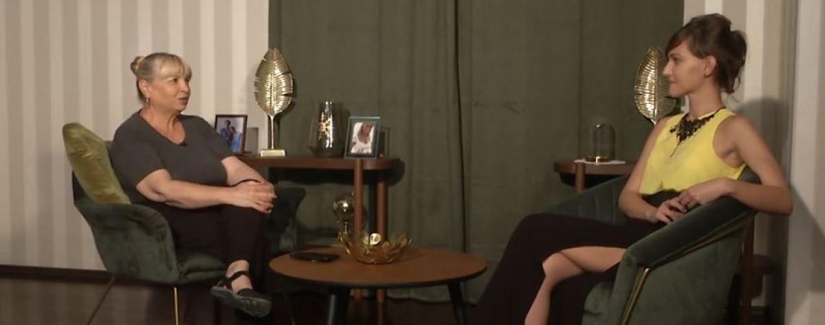 Nuami Dinescu este îmbrăcată în pantaloni negri și o bluză gri și are părul prins cu breton