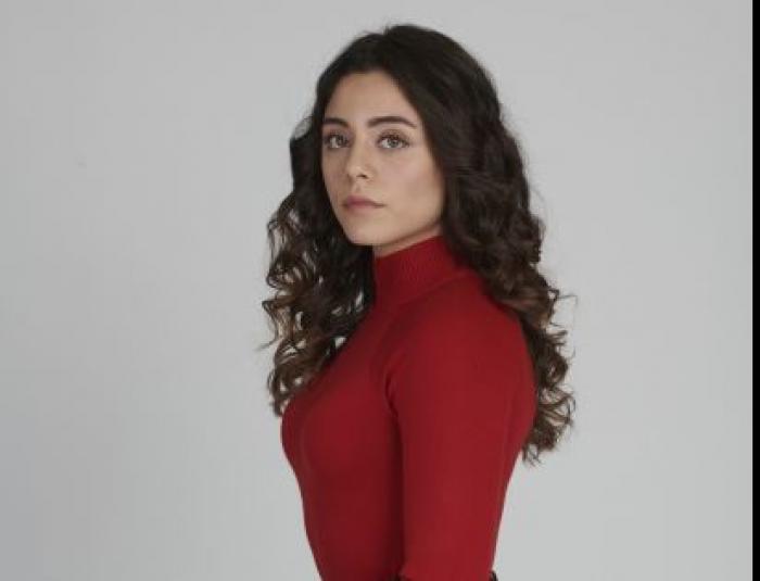 Sila Turkoglu poartă o bluză roșie cu mâneci lungi și are părul desprins și ondulat