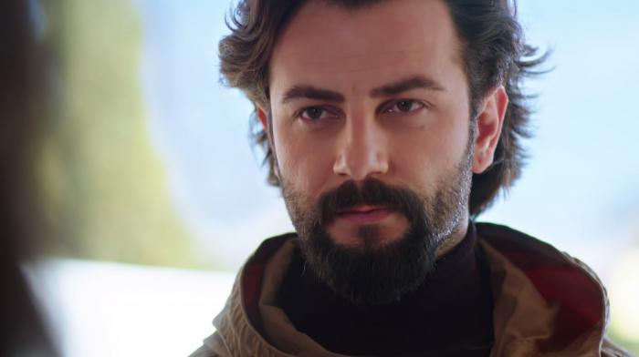 Gokberk Demirci poartă o maletă neagră, pe gât și o geacă maro