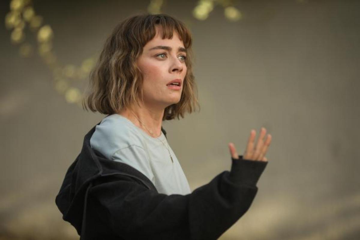 Demet Evgar poartă o bluză albastră și un hanorac negru. Are părul scurt