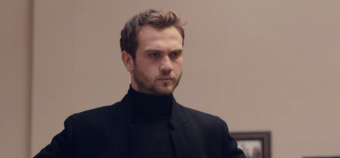 Aras Bulut Iynemli poartă o maletă neagră, pe gât și are un sacou negru