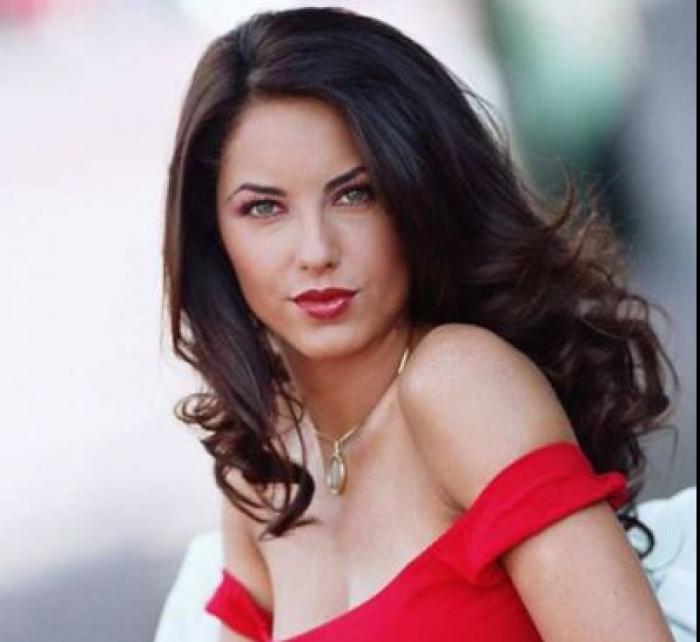 Barbara Mori poartă o rochie roșie cu bretele care îi cad lejer pe umeri. Actrița are părul desprins