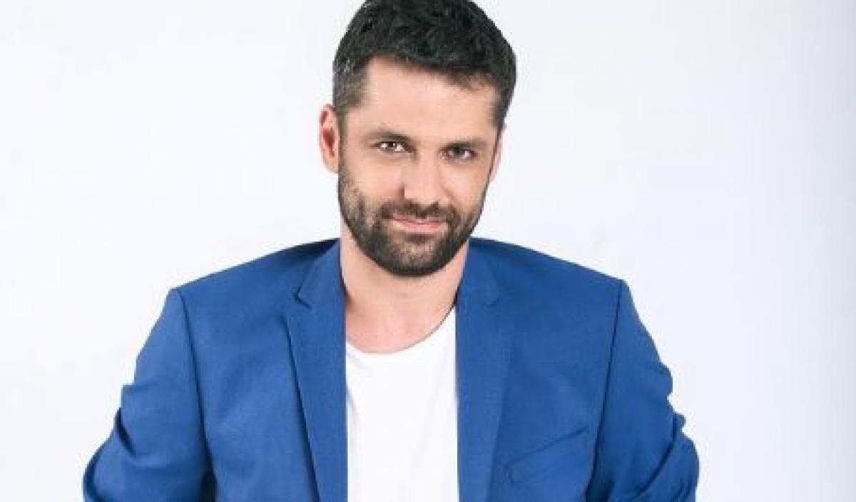 Alecsandru Dunaev este îmbrăcat într-un tricou alb și are un sacou albastru