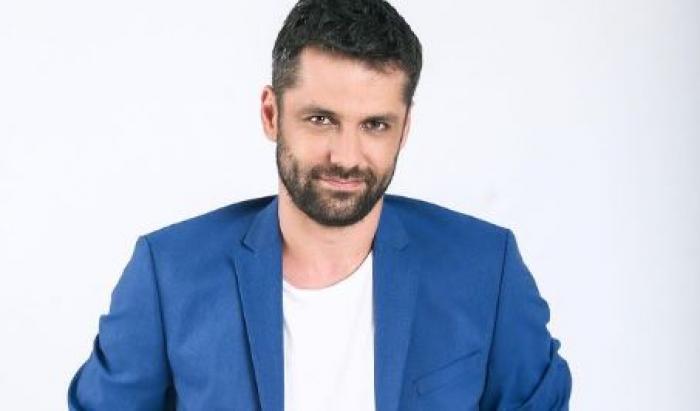 Alecsandru Dunaev este îmbrăcat într-un tricou alb și are un sacou albastru