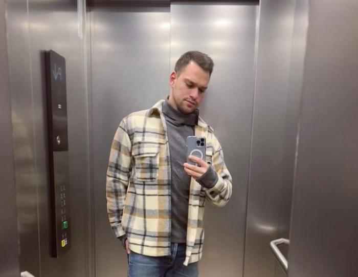 Vlad Gherman poartă blugi albaștri, o maletă gri și o cămașă în carouri