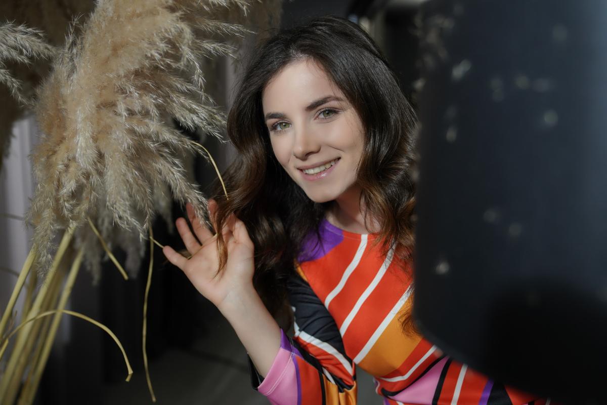 Cansu Tuman poartă o rochie portocalie cu dungi și are părul desprins