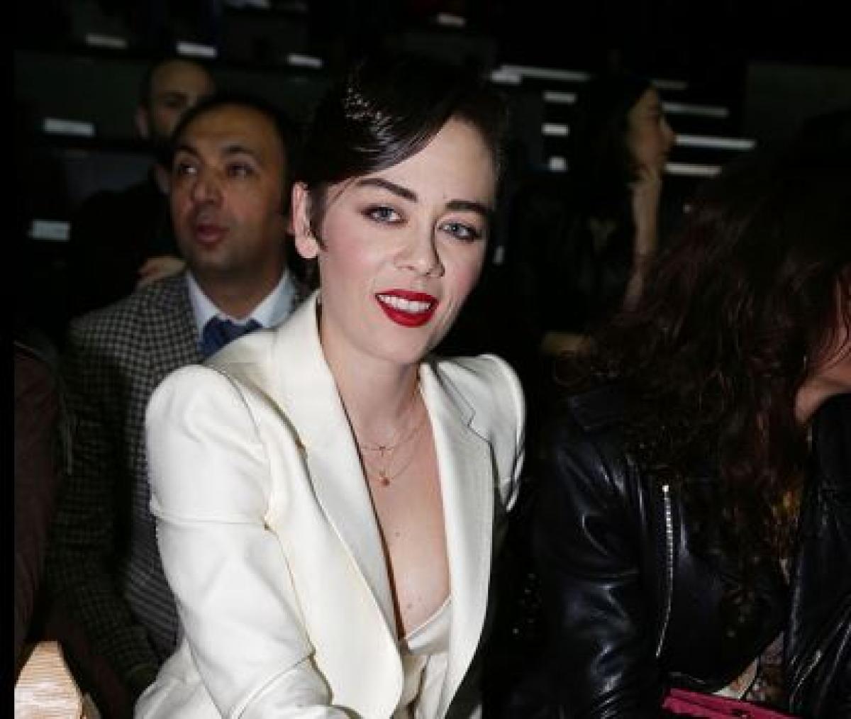 Demet Evgar poartă sacou alb și are părul prins. Actrița poartă un ruj roșu