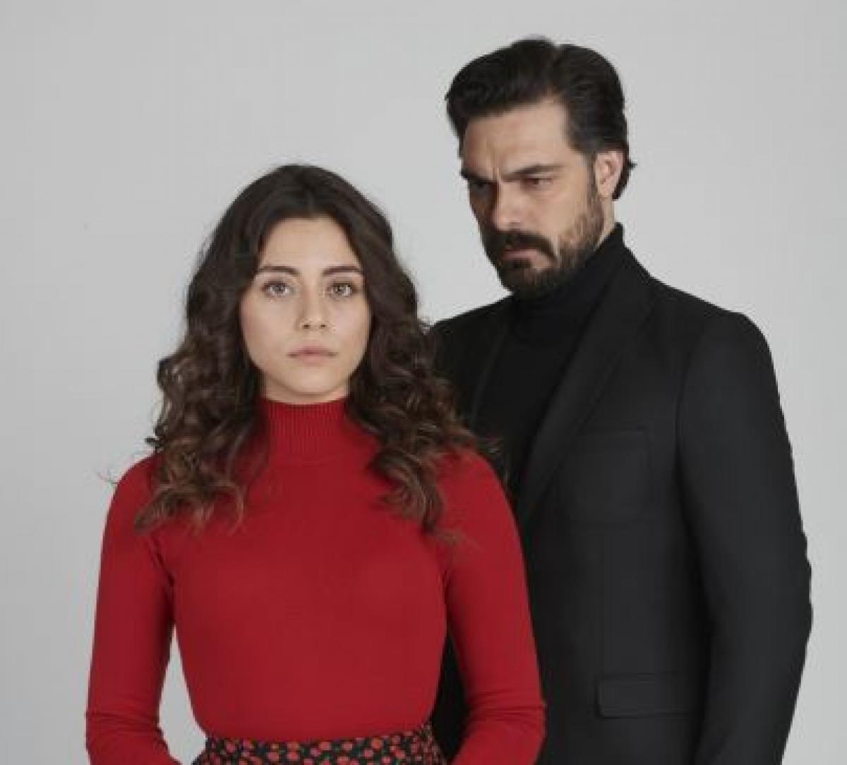 Sila Turkoglu poartă o bluză roșie cu mâneci lungi, iar Halil Ibrahim Ceyhan poartă o maletă neagră și un sacou negru