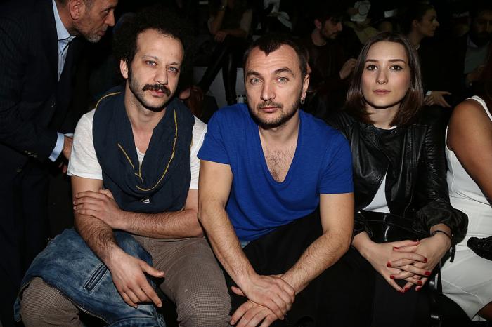 Riza Kocaoglu poartă tricou alb, eșarfă și are păr cârlionțat