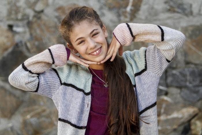 Isabella Damla Guvenilir are părul lung, un tricou vișiniu și un pulover colorat cu dungi