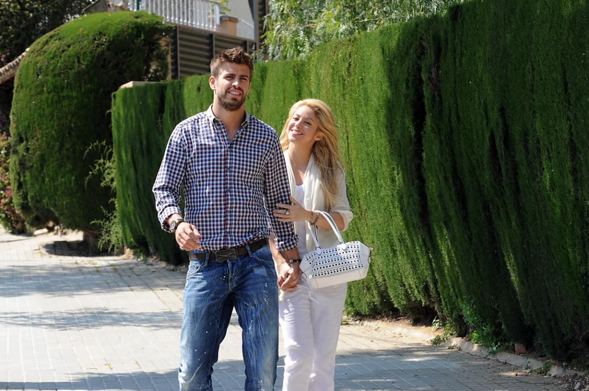 Shakira este îmbrăcată în alb și îl ține de braț pe iubitul ei, Pique. Bărbatul poartă blugi și o cămașă