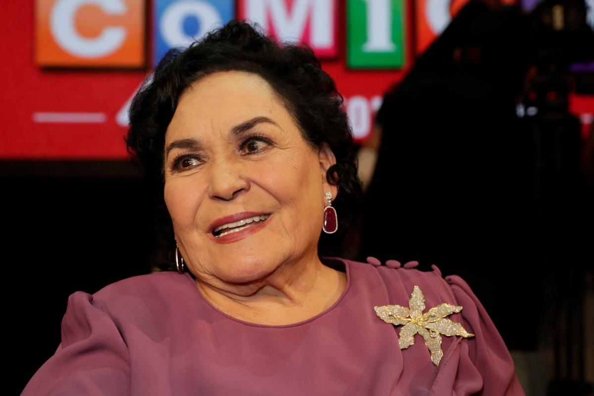 Carmen Salinas poartă o bluză de culoare închisă și are un medalion în piept