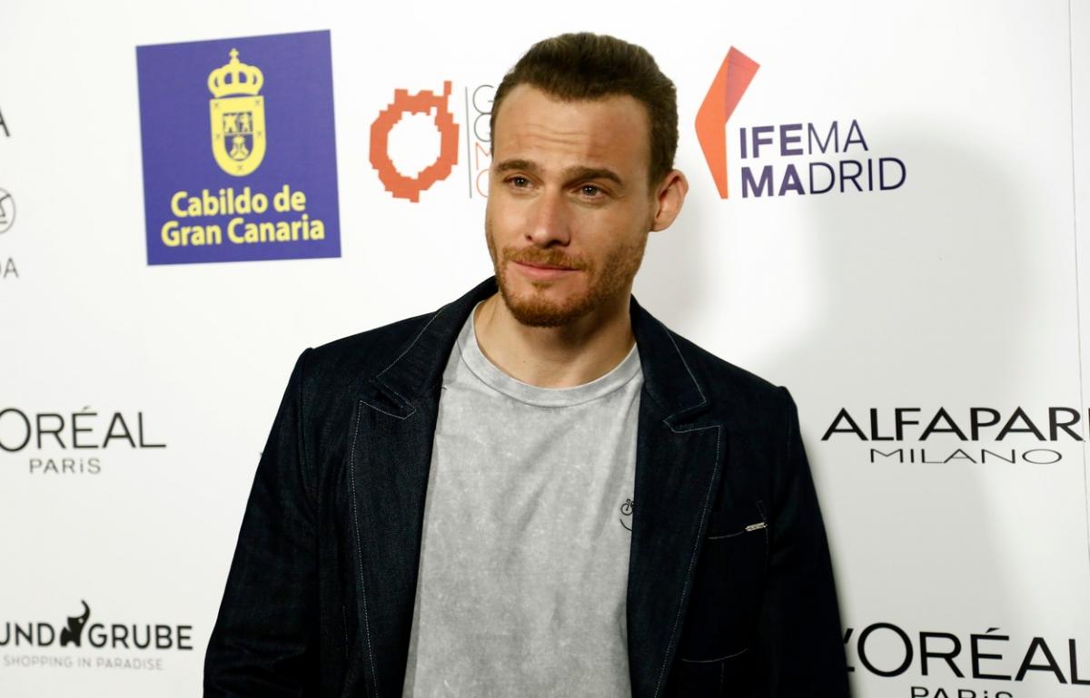 Kerem Bursin poartă un tricou gri și o jachetă neagră