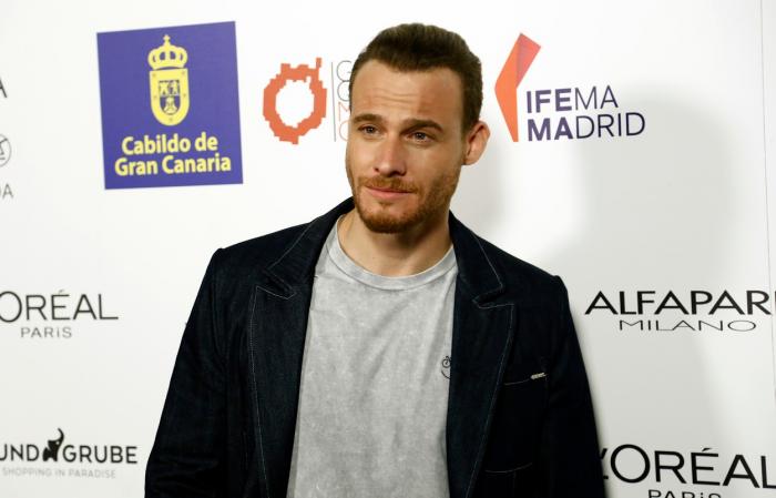 Kerem Bursin poartă un tricou gri și o jachetă neagră