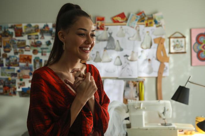 Dilan Cicek Deniz este îmbrăcată într-o bluză portocalie cu imprimeu negru și are părul prins în coadă de cal