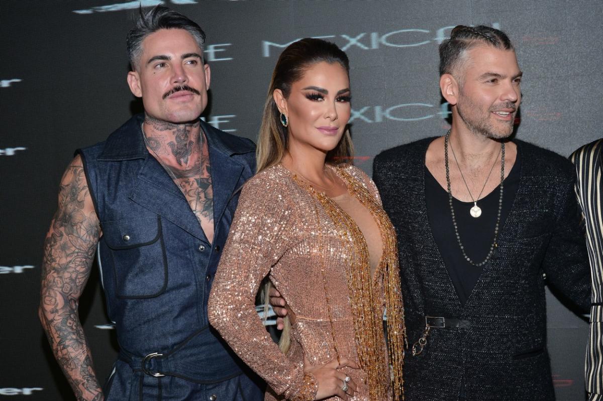 Ninel Conde poartă o rochie de seară și are un machiaj în ton cu evenimentul. Se află între doi bărbați