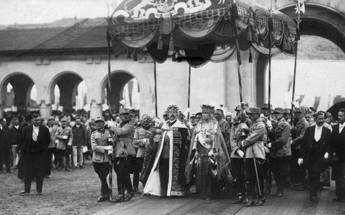 Regele Ferinand merge aproape de Regina Maria. Amândoi poartă coroane pe cap