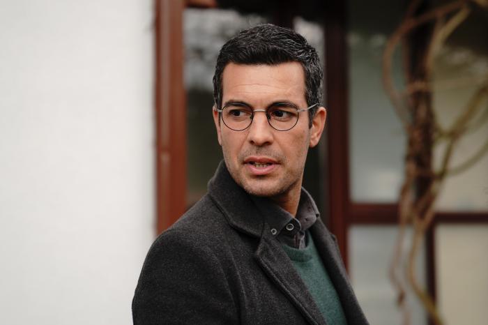 Can Verel poartă o maletă de culoare închisă și are un sacou de aceeași culoare