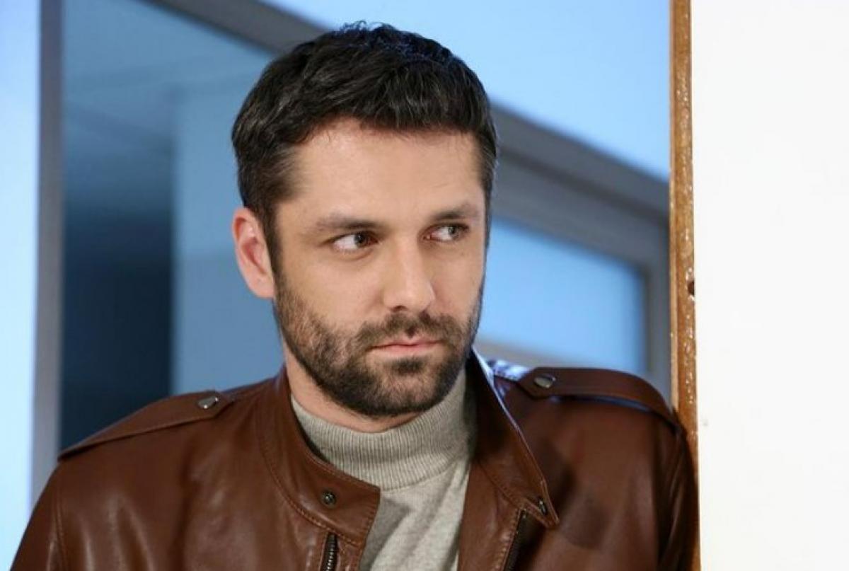 Alecsandru Dunaev poartă o maletă gri și o geacă maro de piele