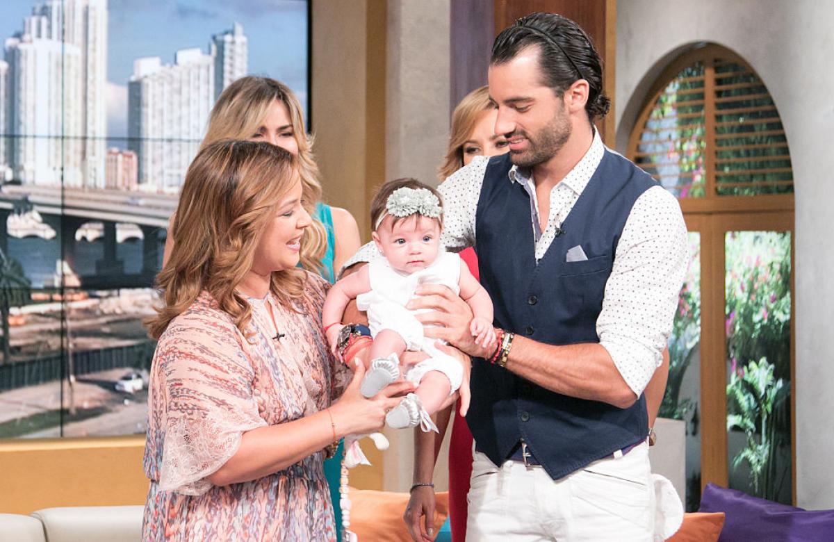 Adamari Lopez poartă o rochie roz, de vară, iar Toni Costa poartă o cămașă albă și o vestă albastru închis. Cei doi își țin fetița în brațe