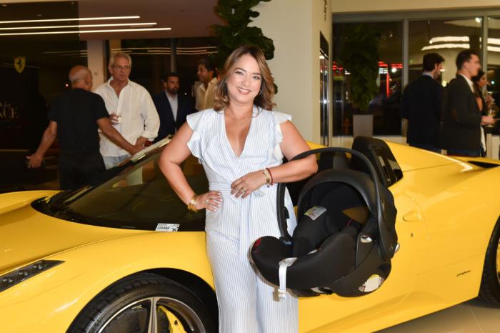 Adamari Lopez poartă un costum alb și ține la braț un scaun de mașină pentru copii
