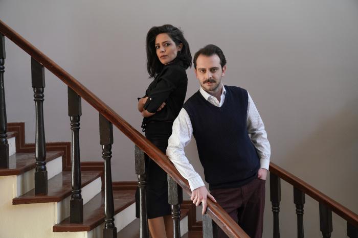 Tolga Pancaroglu poartă o cămașă albă și o vestă neagră și stă alături de Gülay Özdem