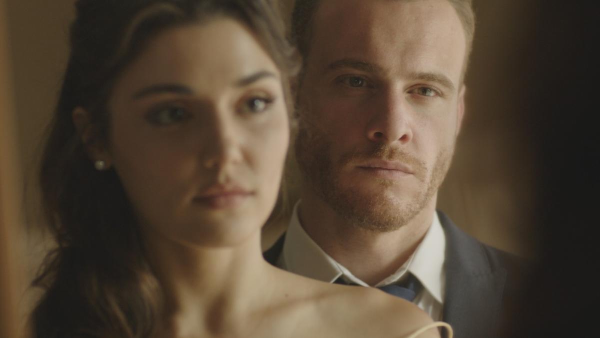 Hande Ercel are părul desprins și stă în fața lui Kerem Bursin care poartă un costum închis la culoare și o cămașă albă