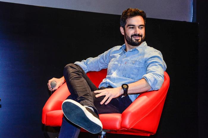 Alfonso Herrera poartă pantaloni închiși la culoare și o cămașă albastră