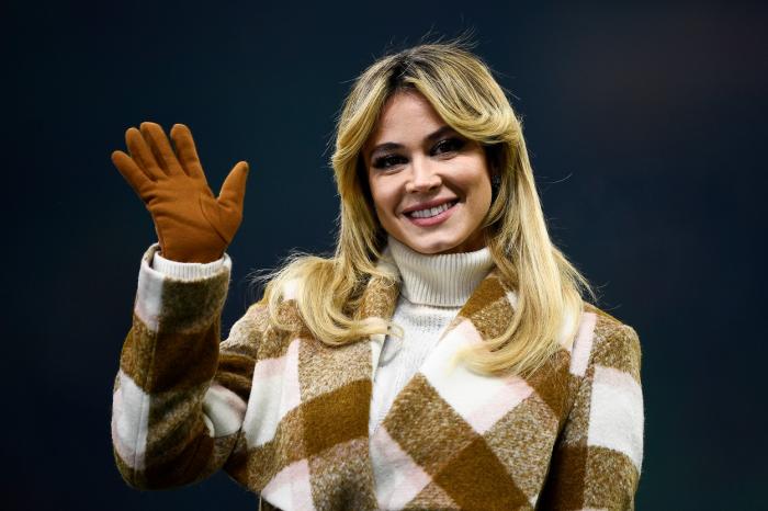 Diletta Leotta poartă o maletă albă pe gât, are un palton alb cu maro și poartă mănuși maro, groase. Jurnalista are părul desprins