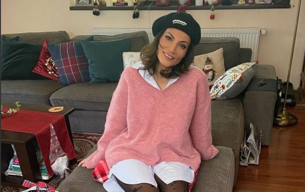 Ioana Ginghină poartă o cămașă albă și un pulover roz. Are o bască neagră pe cap