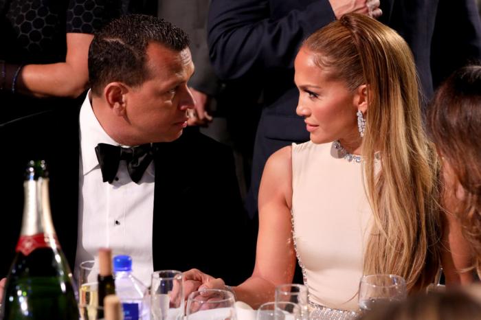 Alex Rodriguez poartă un costum negru și stă la masă lângă JLo