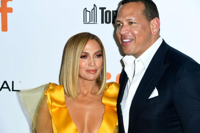 Alex Rodriguez poartă un costum închis la culoare și are o cămașă albă. JLo are o rochie galbenă cu decolteu și părul scurt