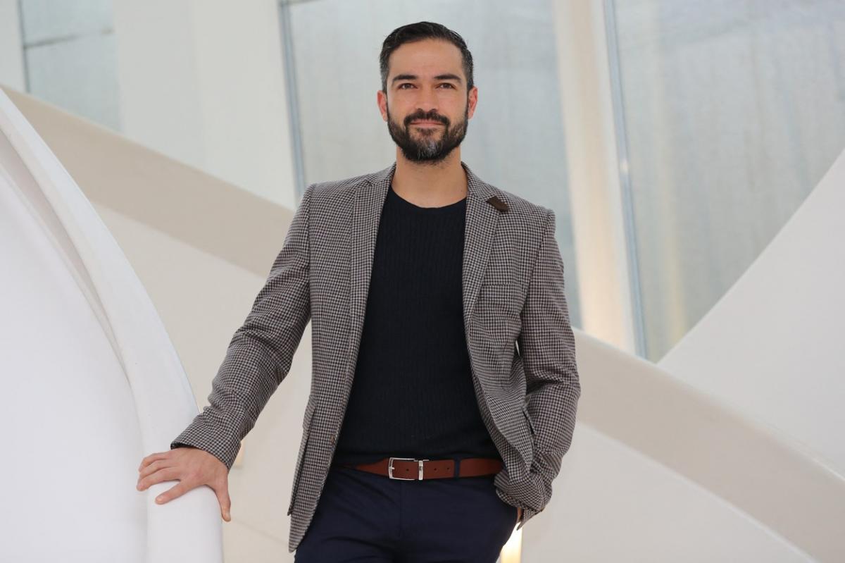 Alfonso Herrera poartă blugi închiși la culoare, bluză neagră și sacou gri