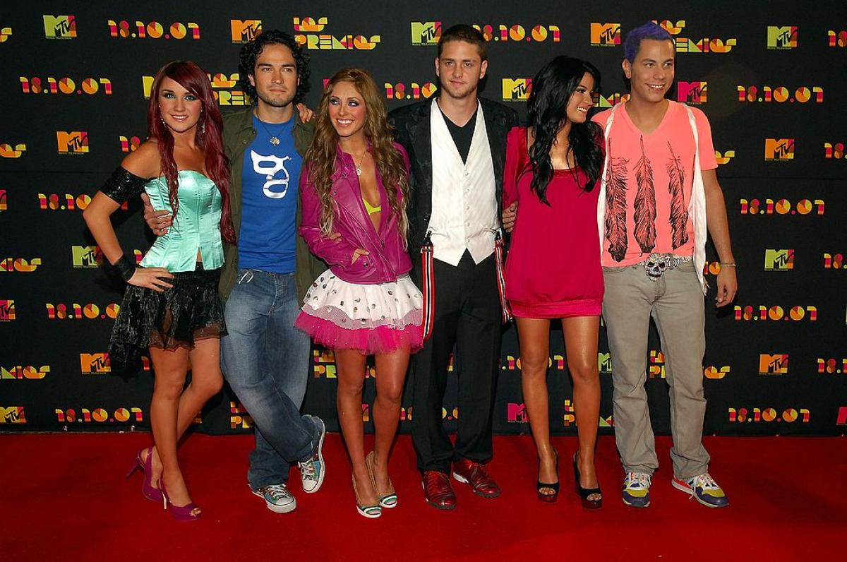 Dulce Maria stă lângă Alfonso Herrera și poartă o fustă neagră și un corset azuriu