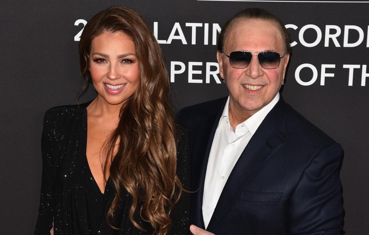 Thalia este îmbrăcată într-o rochie neagră, cu decolteu și are părul desprins și ondulat. Tommy Mottola poartă o cămașă albă și un sacou negru și are ochelari de soare