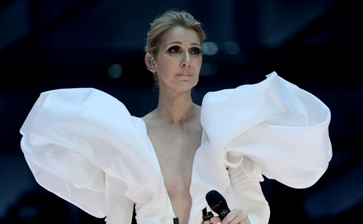 Celine Dion poartă o rochie albă cu volane largi și are un machiaj de seară