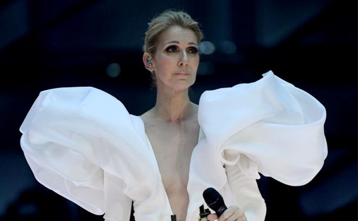 Celine Dion poartă o rochie albă cu volane largi și are un machiaj de seară