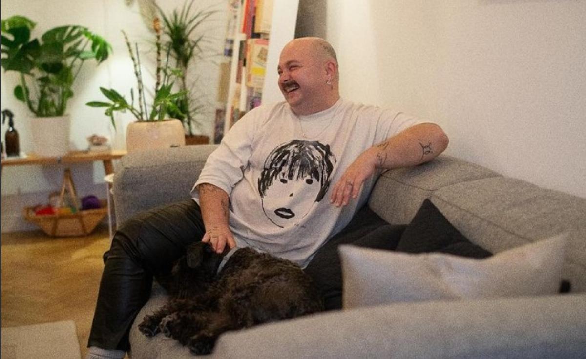 Zarug poartă un tricou cu un imprimeu și stă pe o canapea lângă un câine